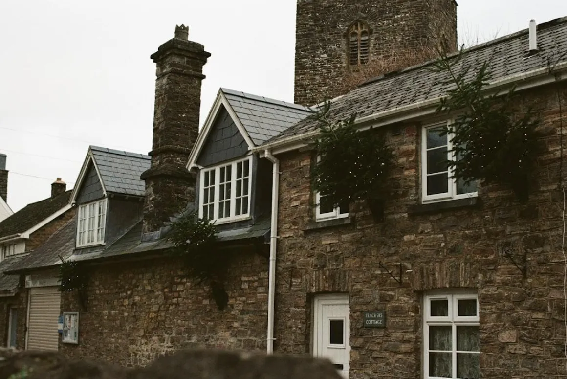 Person on a ladder clearing gutters on a rural stone cottage